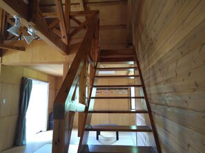 A wooden interior with a staircase, wooden beams, and a window with a curtain.