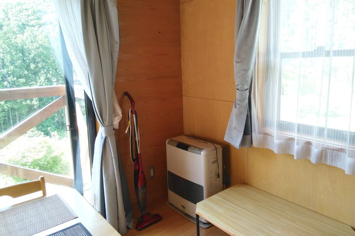 Une pièce avec un plancher en bois, une petite table, une chaise, un radiateur et une fenêtre avec des rideaux.