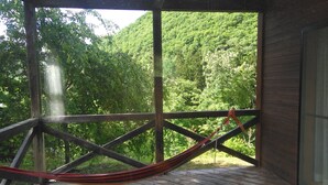 Um deck de madeira com uma rede e vista para uma encosta arborizada.