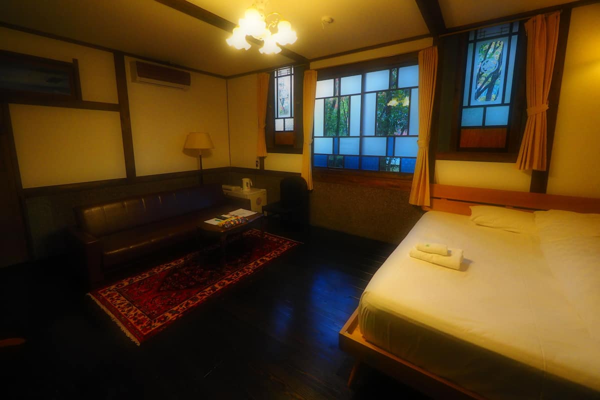 Habitación de hotel con cama, sofá, mesita, lámpara y ventana con cortinas.