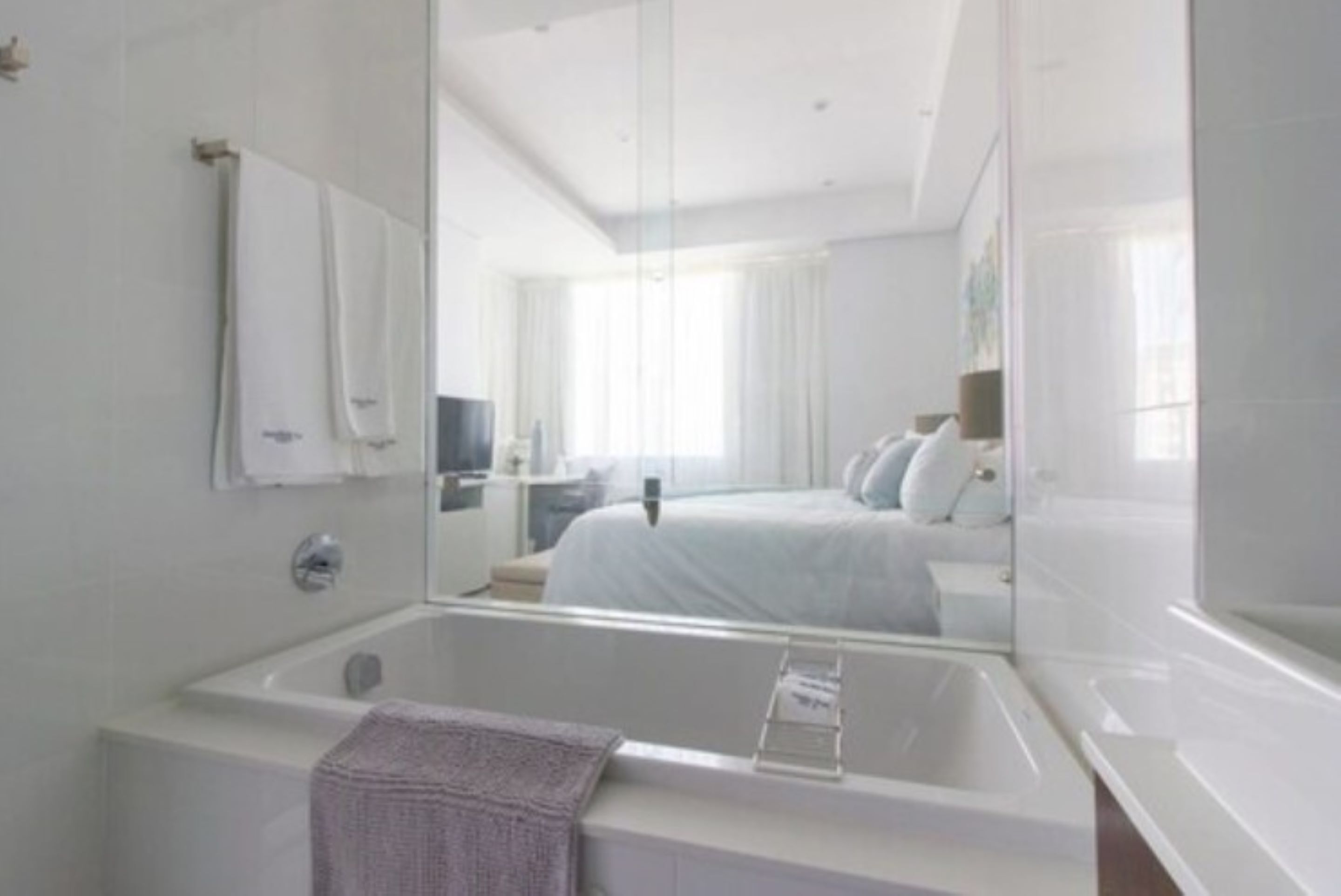 Una habitación de hotel moderna con un espejo grande, una bañera y una cama bien tendida.