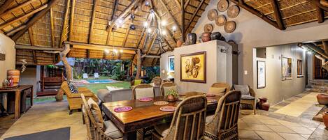 A dining area with a wooden table, wicker chairs, and a thatched roof ceiling.