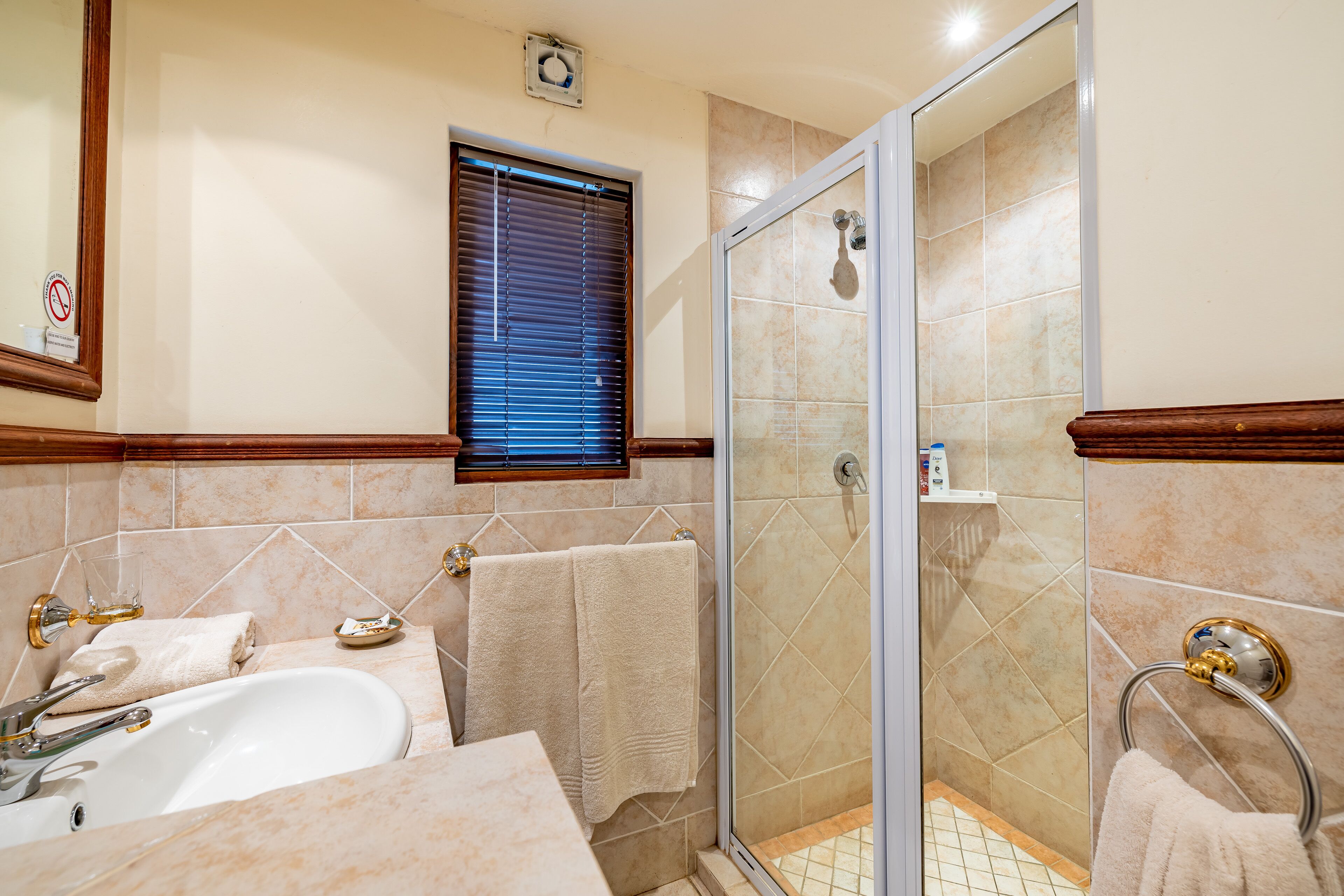 A bathroom with a glass-enclosed shower, a sink, and a window with blinds.