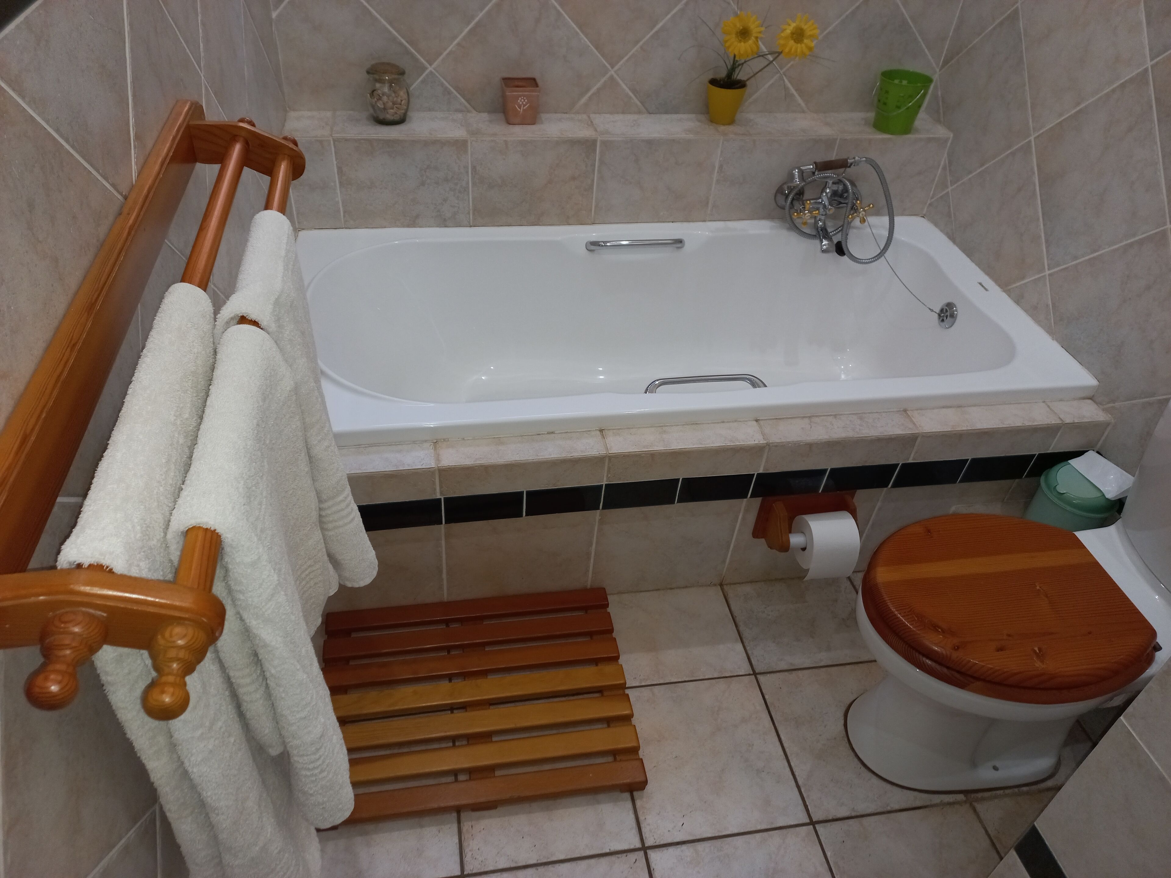 A bathroom with a bathtub, toilet, wooden towel rack, and a shelf with decorative items.
