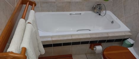 A bathroom with a bathtub, toilet, wooden towel rack, and a shelf with decorative items.