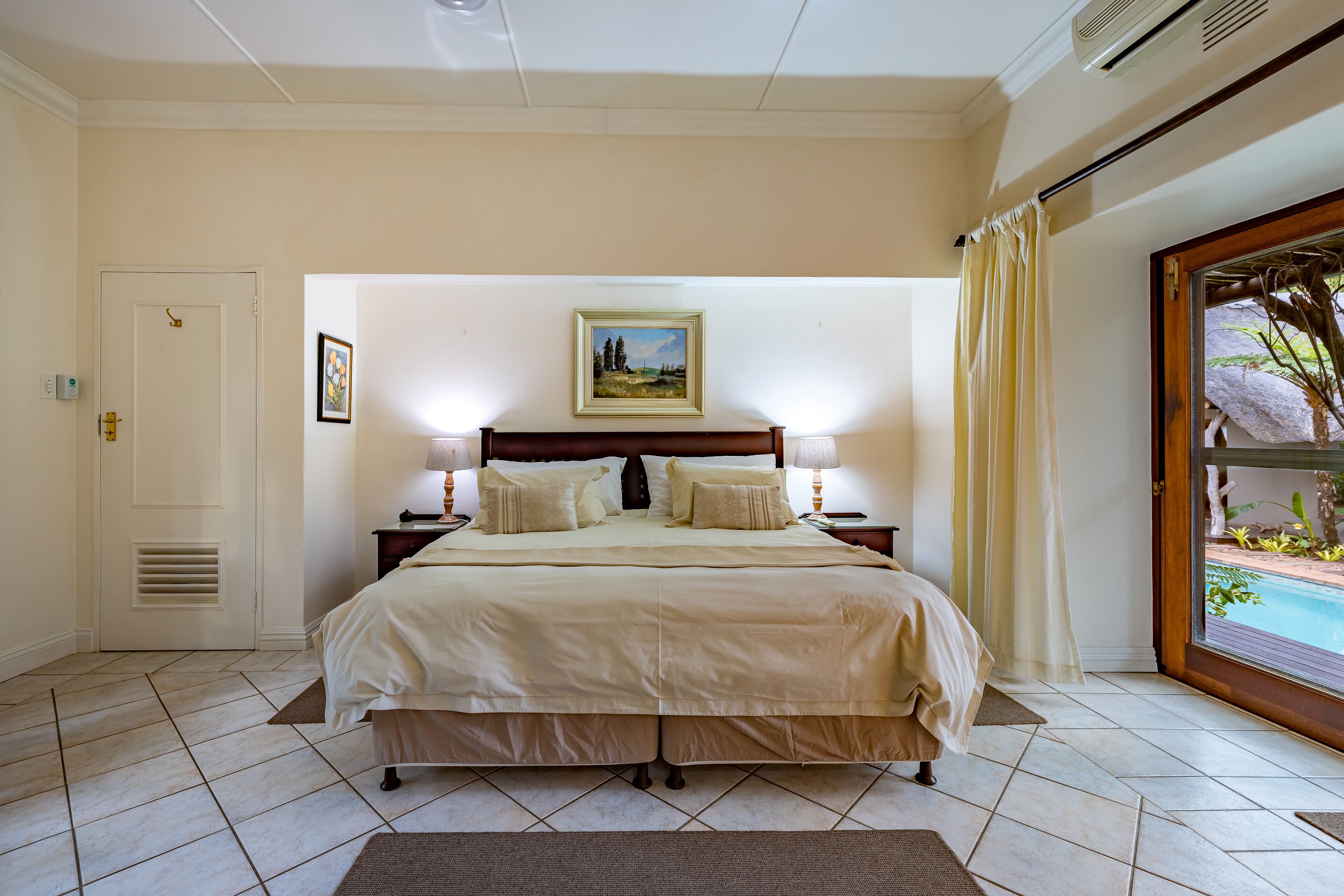 Ein Schlafzimmer mit einem großen Bett, einem Gemälde an der Wand und Blick auf einen Pool durch eine Glastür.