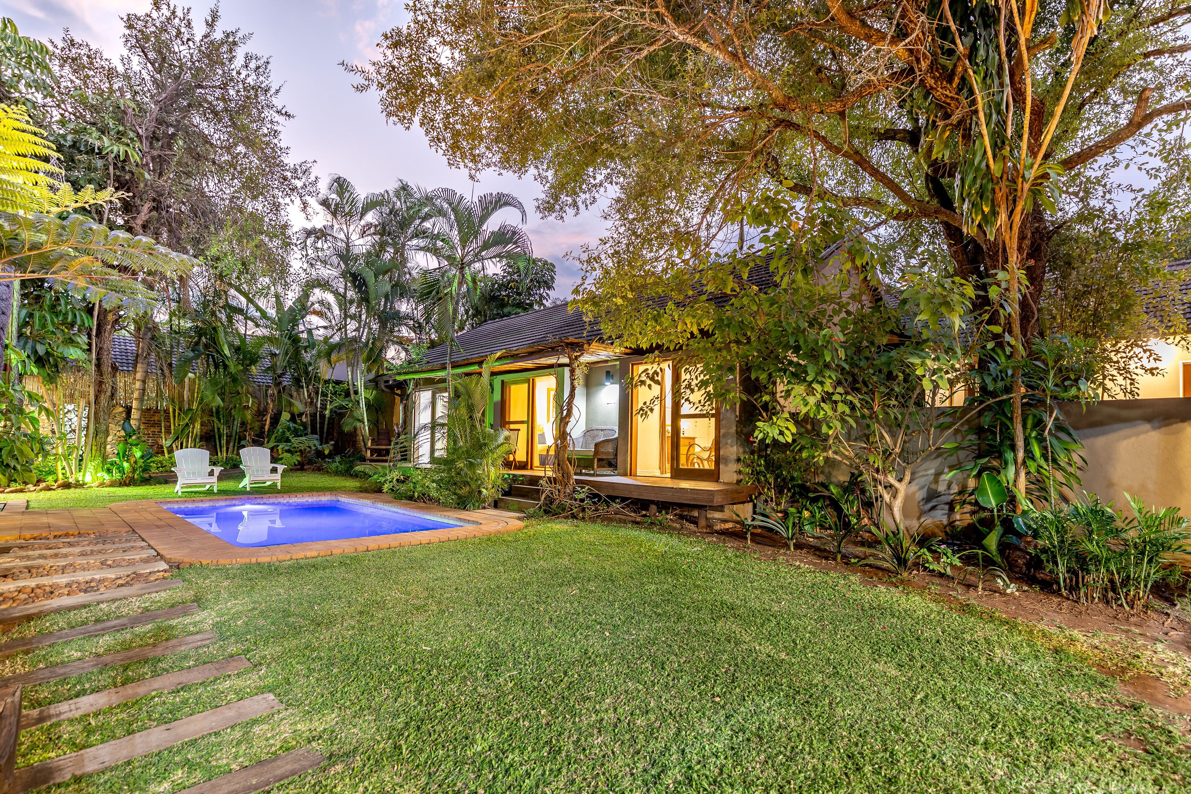 A backyard with a swimming pool, a wooden deck, and a small house with a porch.