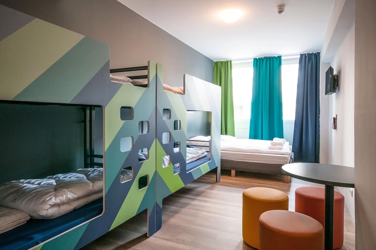 Een moderne hotelkamer met stapelbedden, een klein rond tafeltje en uitzicht op zee door grote ramen.