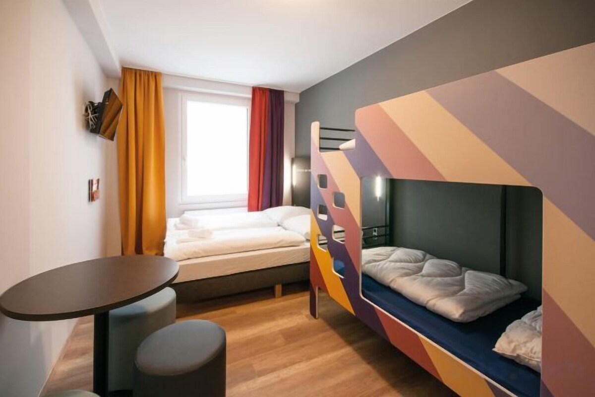 Une chambre avec un lit superposé, une petite table et une fenêtre avec des rideaux.