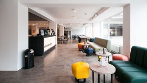 Eine moderne Hotelhalle mit Empfangsschalter, Sitzbereichen und großen Fenstern.