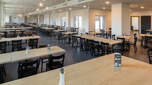 Eine geräumige Cafeteria mit mehreren Tischen und Stühlen, hohen Decken und Pendelleuchten.
