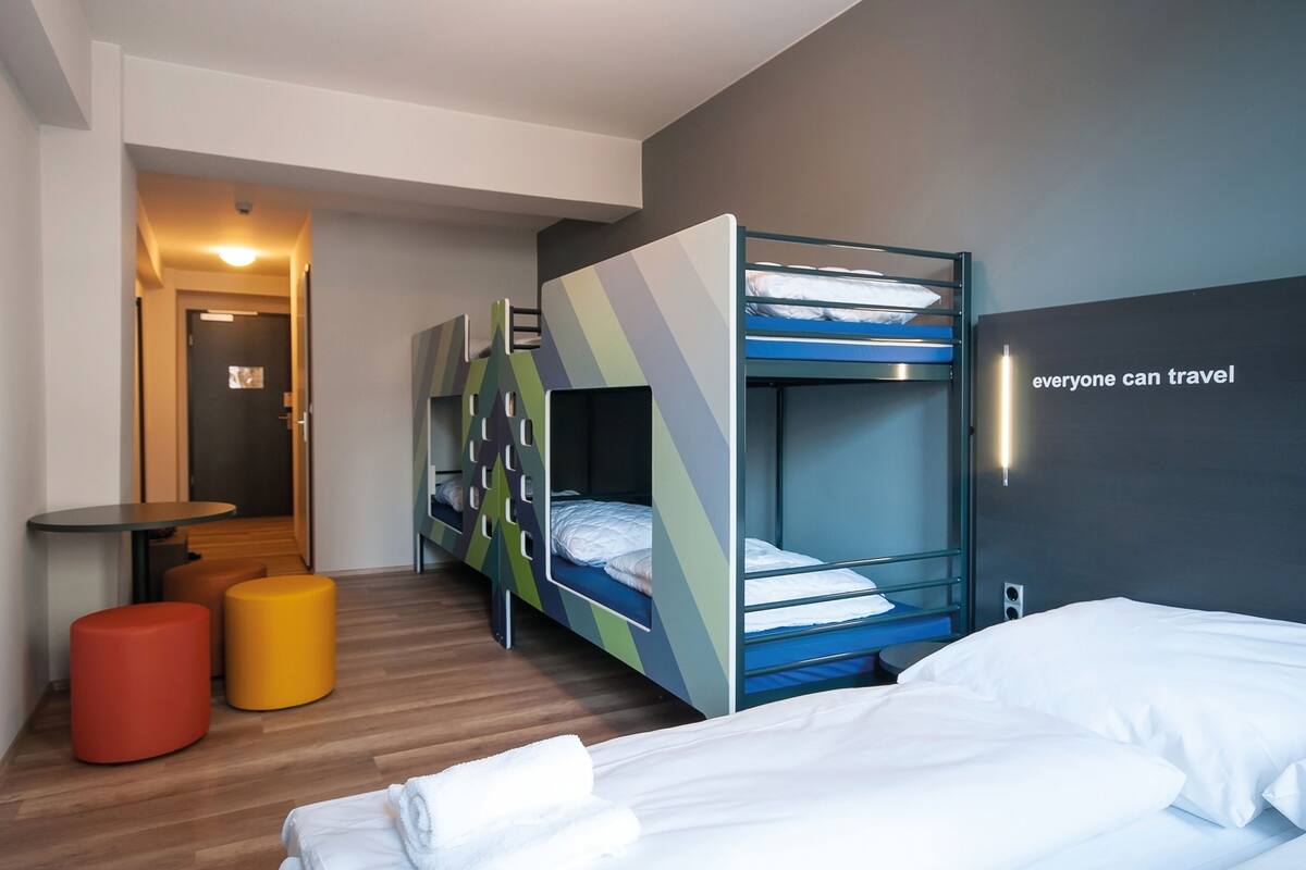 Een moderne hotelkamer met stapelbedden, een tafeltje en twee poefs.