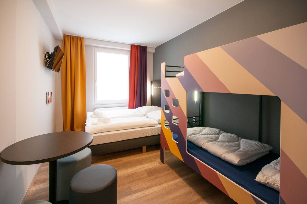 Een moderne kamer met een stapelbed, een klein rond tafeltje en een raam met gordijnen.
