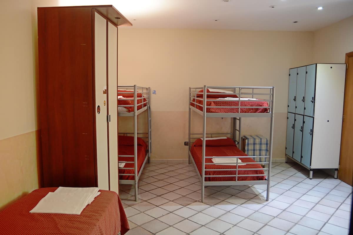 A dormitory room with bunk beds, a wardrobe, and a tiled floor.