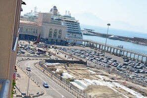 A large cruise ship docked at a port with a busy parking area and a bridge in the background. - Ostello Bella Napoli (Naples)
