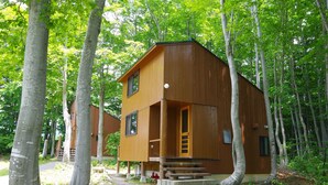 A wooden cabin with a front porch and steps, surrounded by trees. - Gassan Pole Pole Farm (Nishikawa)