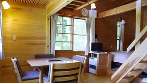 A wooden cabin interior with a dining table, chairs, a television, and a staircase. - Gassan Pole Pole Farm (Nishikawa)