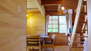A wooden cabin interior with a dining table, chairs, a window with curtains, a clock, and a staircase. - Gassan Pole Pole Farm (Nishikawa)