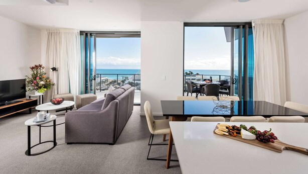 A modern hotel room with a living area, a dining table with a fruit platter, a sofa, and a TV. - Ramada VetroBlu Scarborough Beach (Scarborough)