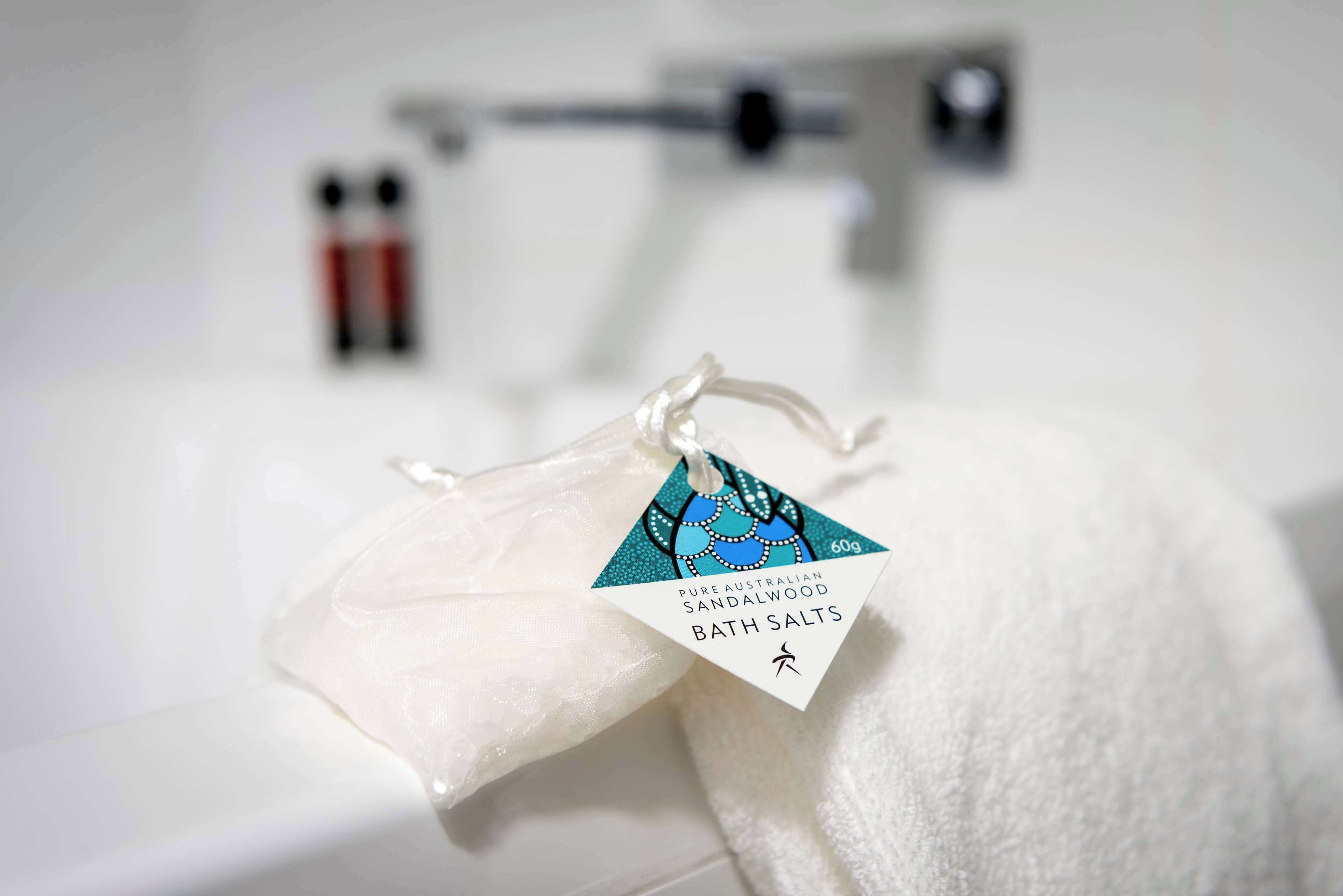 Een witte badmat met een etiket waarop staat: 'Pure Australian Sandalwood Bath Salts'.