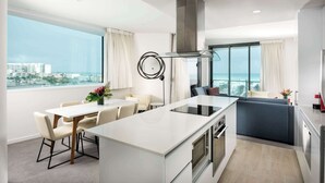 A modern kitchen with a central island, a dining area with a table and chairs, and a view of the ocean. - Ramada VetroBlu Scarborough Beach (Scarborough)