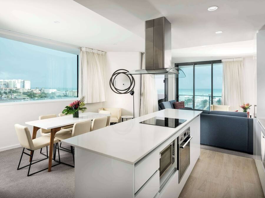 Una cocina moderna con una isla central, un comedor con mesa y sillas, y vista al océano.