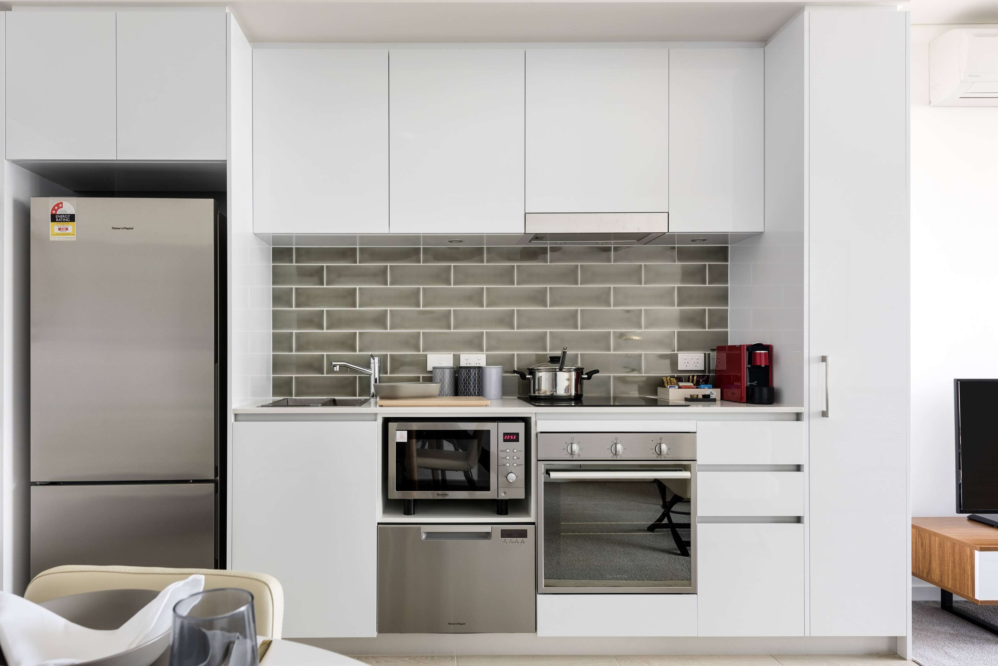 A modern kitchen with white cabinets, a stainless steel refrigerator, a built-in oven, and a microwave.
