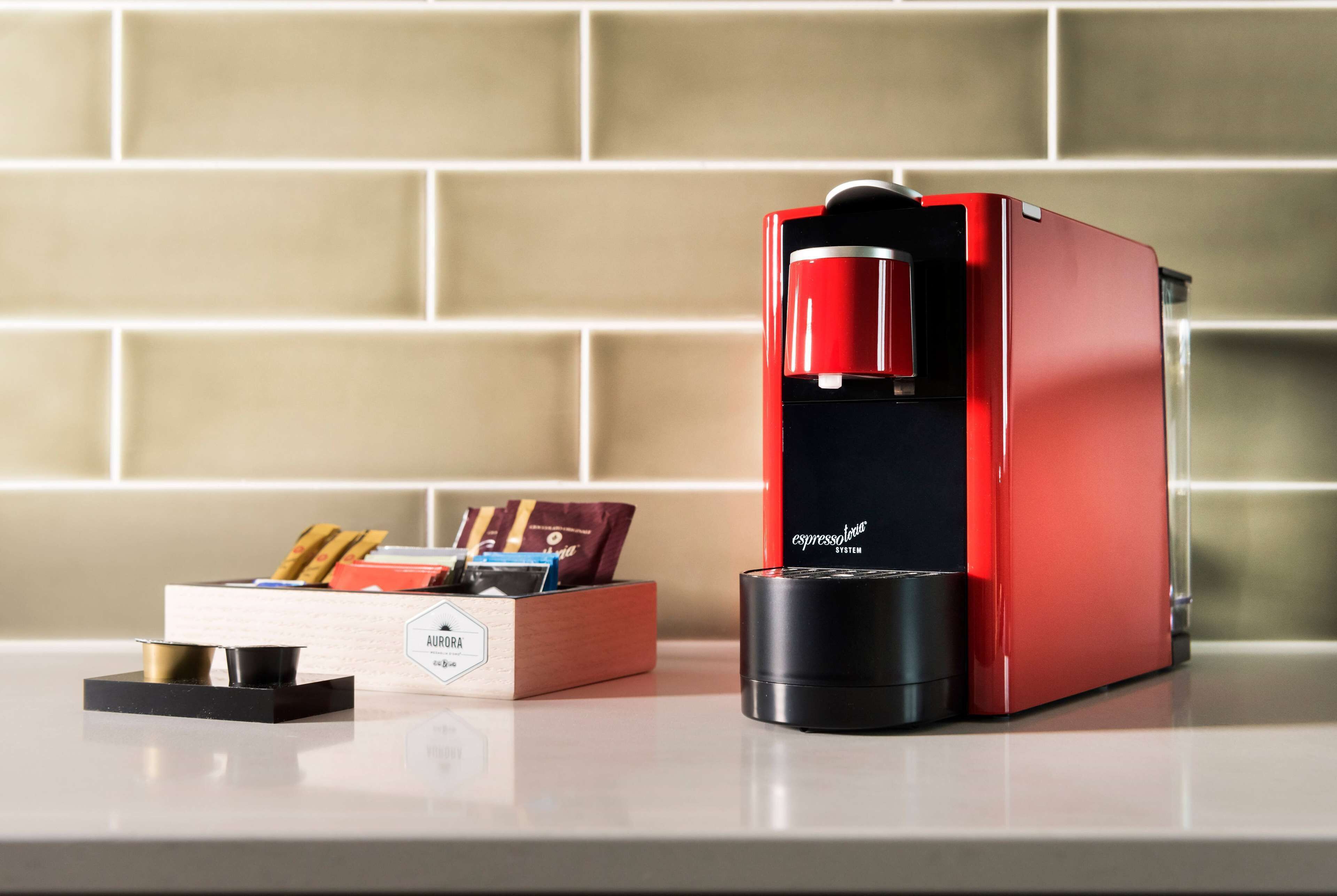Una cafetera roja con base negra, una caja de madera con cápsulas de café y un recipiente negro con enchufe.