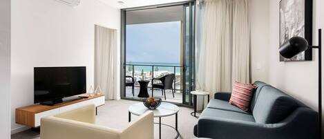 Ein modernes Wohnzimmer mit Fernseher, Sofa, Couchtisch und einem Balkon mit Meerblick.