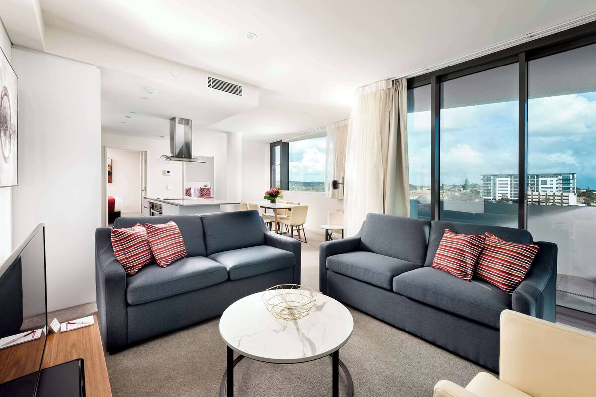 A modern living room with two grey sofas, a white coffee table, and a view of the city through large windows.