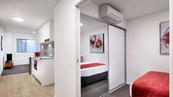 A compact hotel room with a kitchenette, a bed with a red blanket, and a sliding door closet.