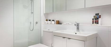 Un baño moderno con ducha de vidrio, inodoro, lavamanos y espejo sobre el lavamanos.