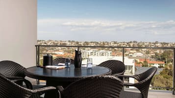 Ein runder Tisch mit Korbstühlen auf einem Balkon mit Blick auf eine Stadtlandschaft.