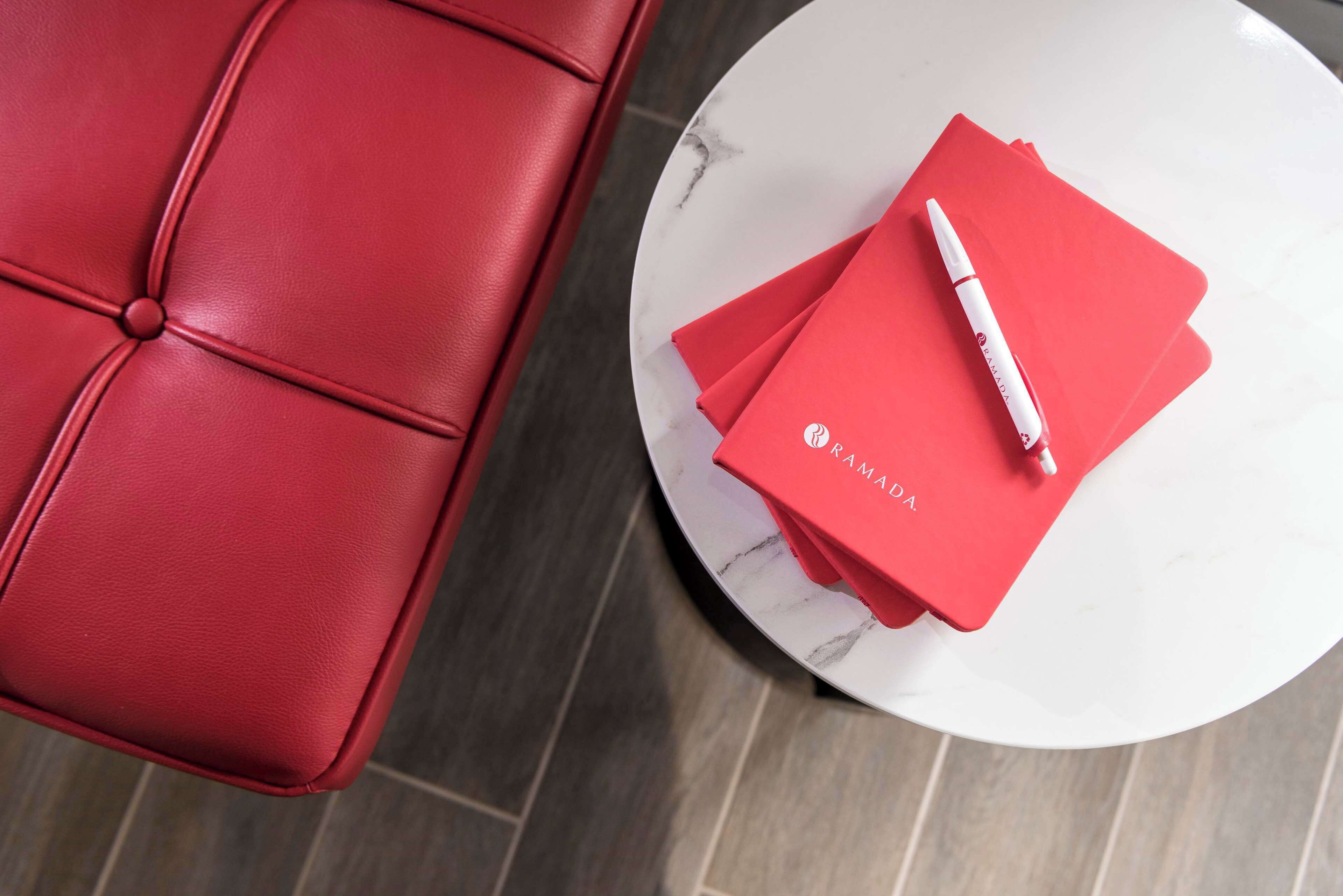 A red leather sofa and a white marble table with red folders and a pen.