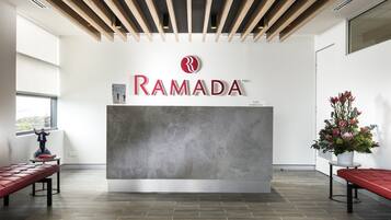 A reception area with a modern design, featuring a reception desk with a logo, a bench, and a potted plant.