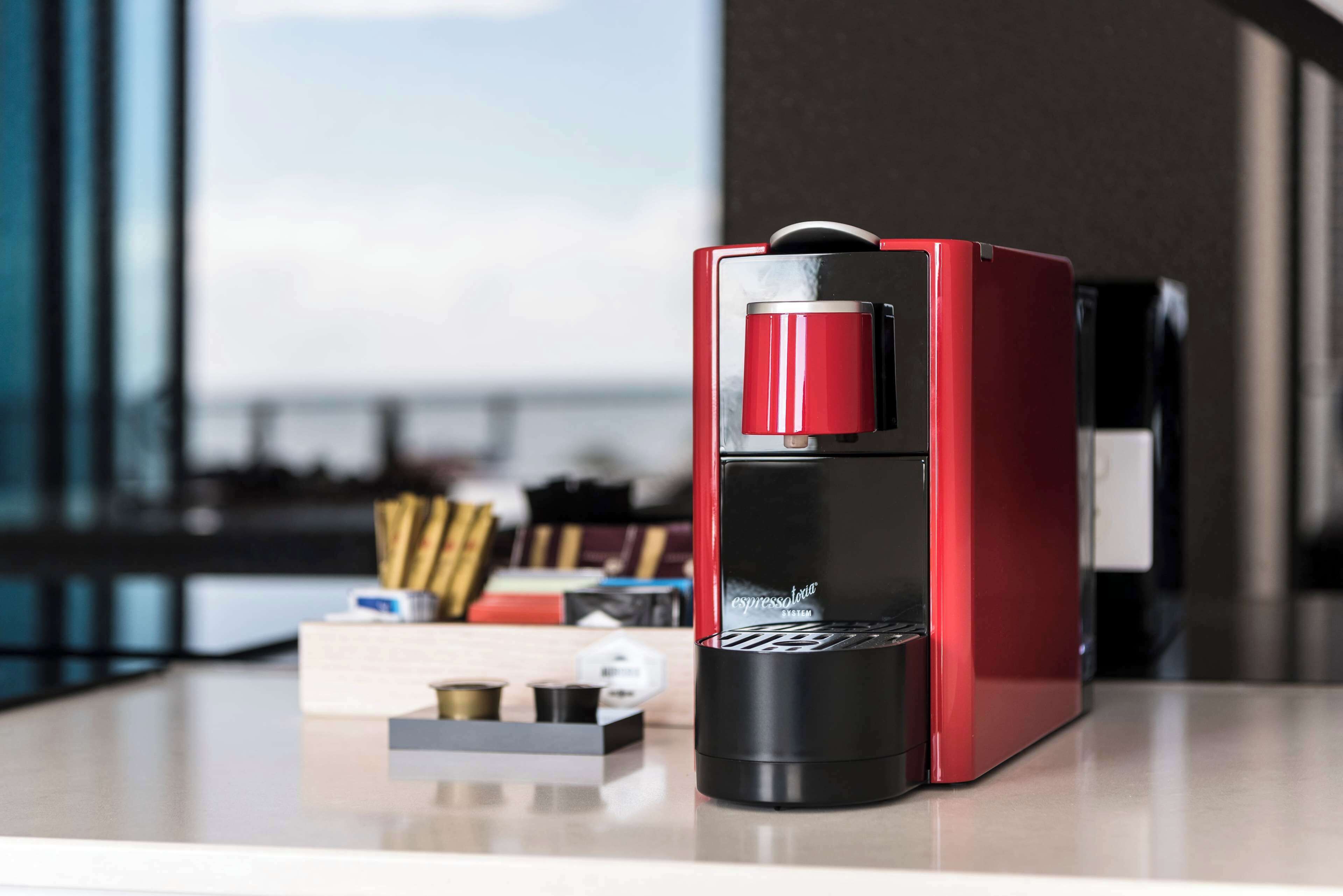 Una máquina de espresso roja y negra sobre una encimera con vistas a una ventana.