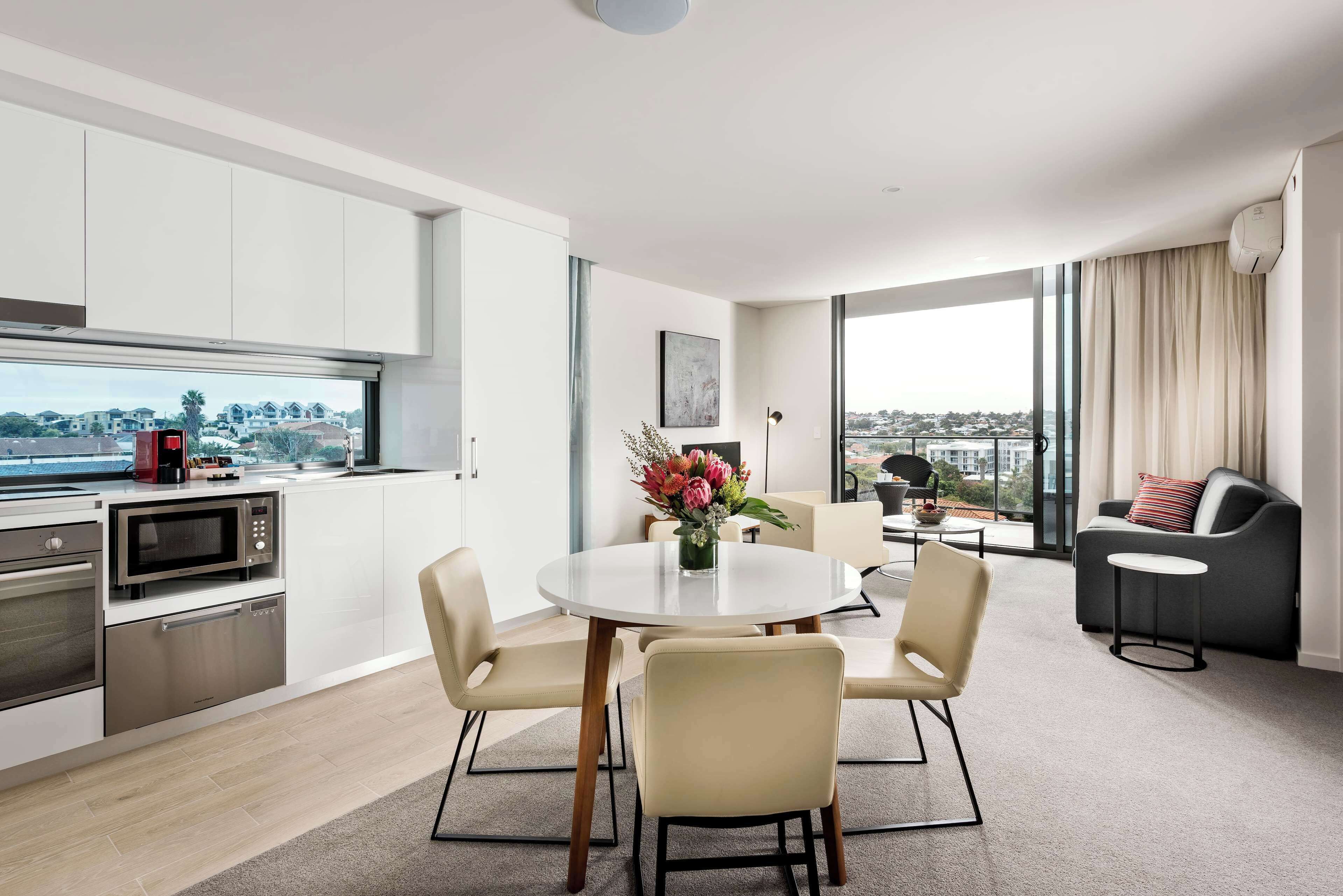 A modern kitchen with integrated appliances, a dining area with a round table and chairs, and a seating area with a sofa and a small table.