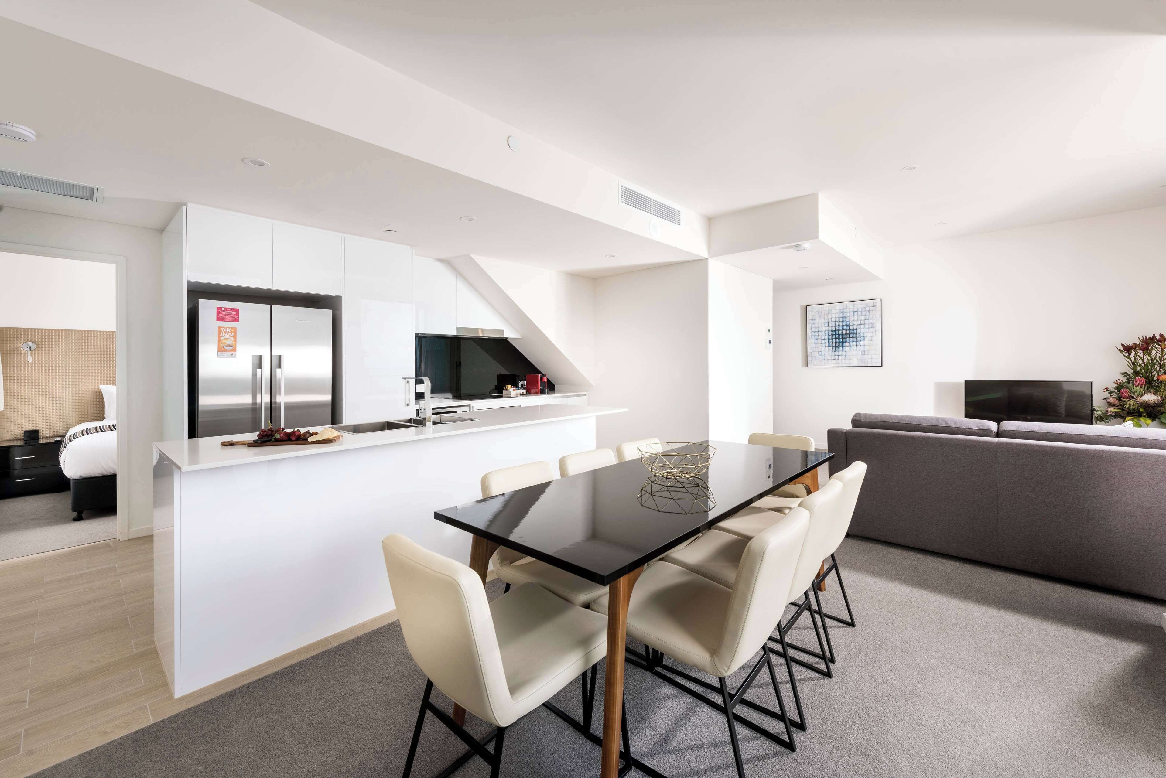 A modern living space with a central island dining table, a grey sofa, and a flat-screen TV.
