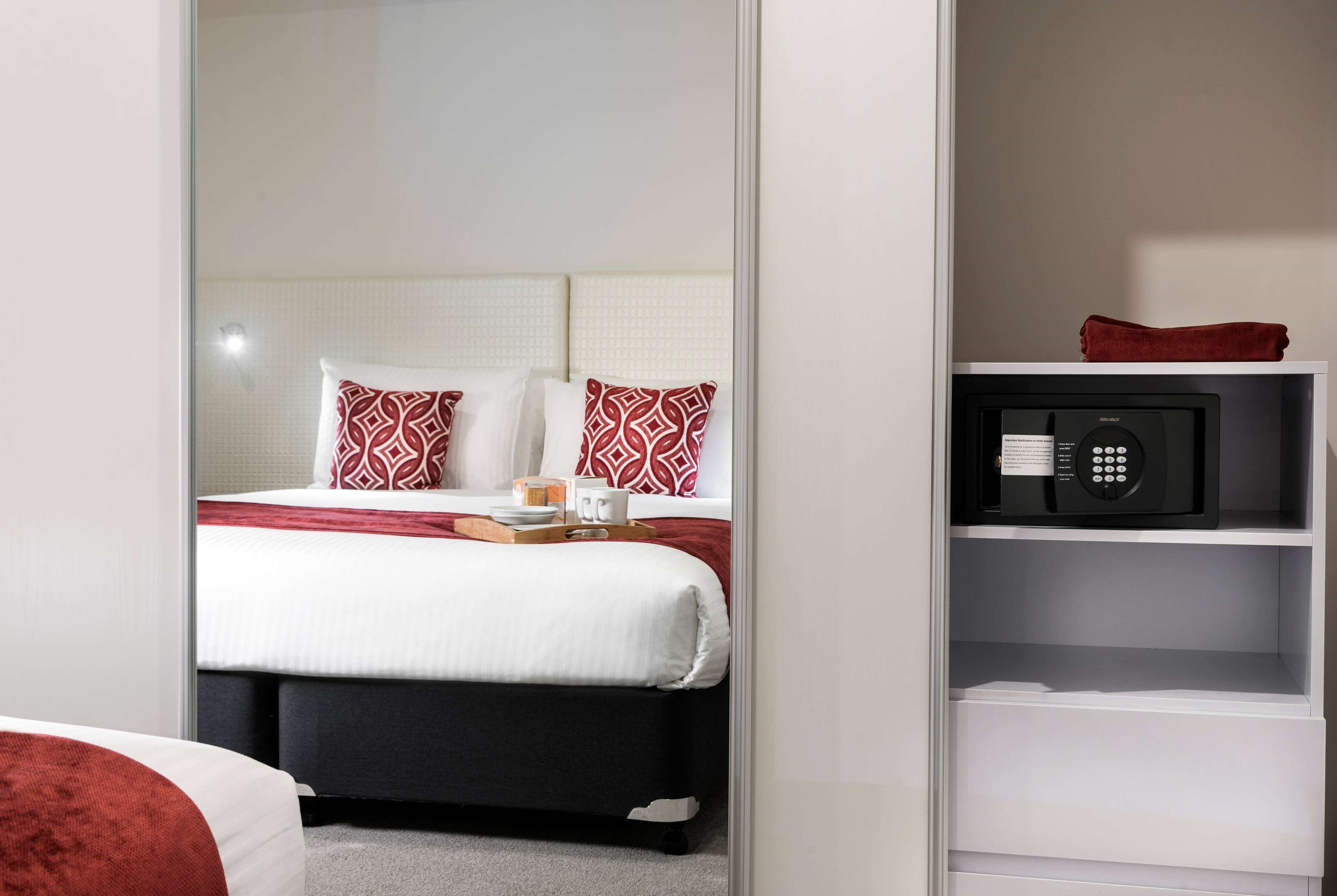 Una habitación de hotel con una cama bien hecha, un microondas en un estante y una mesita con una bandeja.