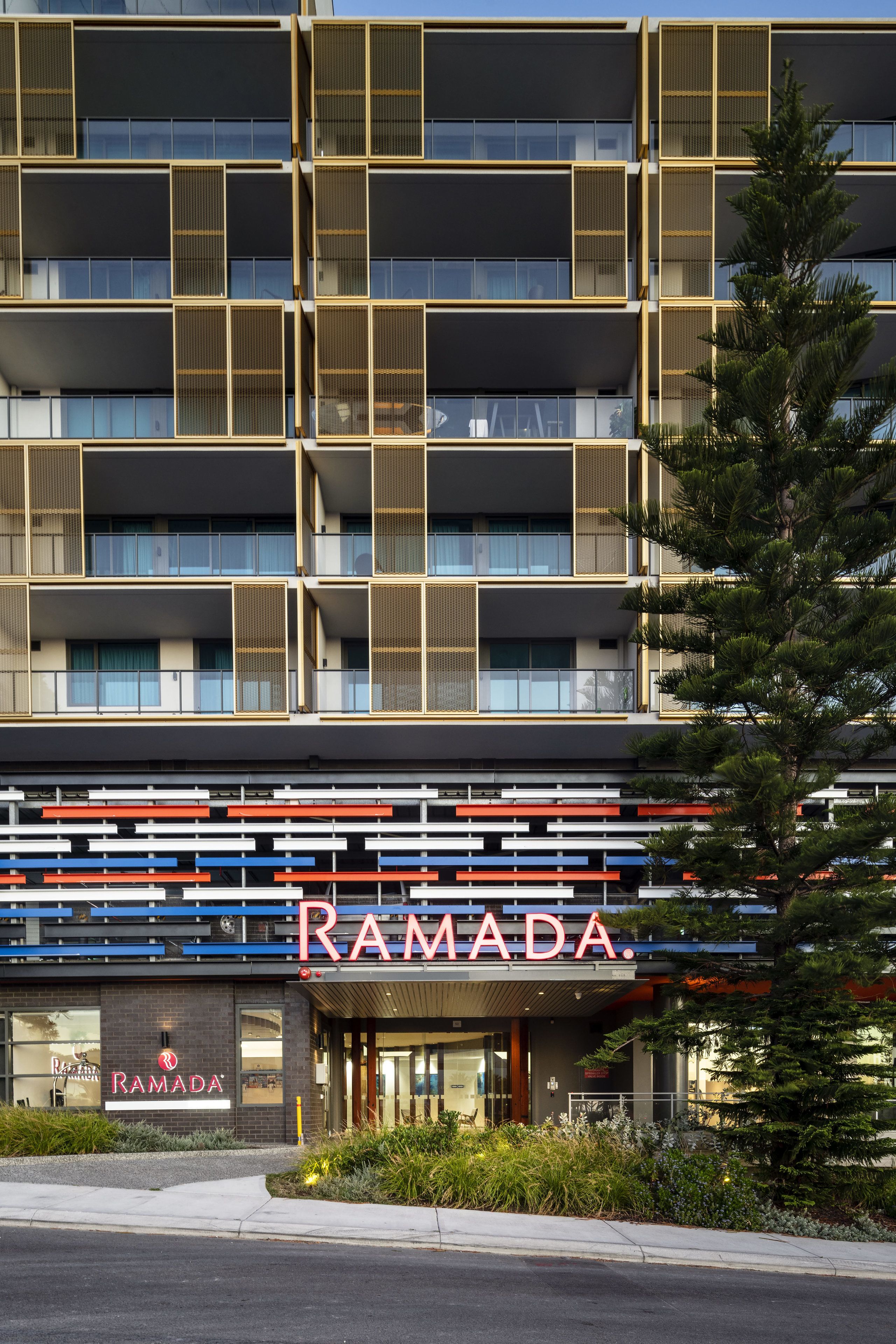 A multi-story building with a modern facade, featuring balconies with mesh railings and a prominent 'RAMADA' sign at the ground level.