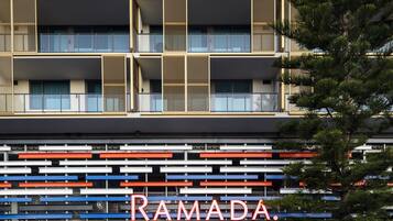 A multi-story building with a modern facade, featuring balconies with mesh railings and a prominent 'RAMADA' sign at the ground level.