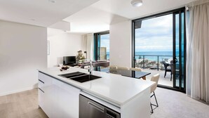 A modern kitchen with a central island, a dining area with a table and chairs, and a balcony with a view of the sea. - Ramada VetroBlu Scarborough Beach (Scarborough)