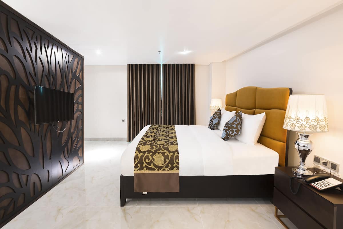 Ein modernes Hotelzimmer mit einem großen Bett, einem dekorativen Kopfteil, einem Nachttisch mit Lampe und einem am Wand montierten Fernseher.