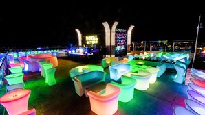 Eine Dachterrasse mit farblich beleuchteten Sitzgelegenheiten und einer Neonreklame mit dem Schriftzug "ROYAL SKYBAR".