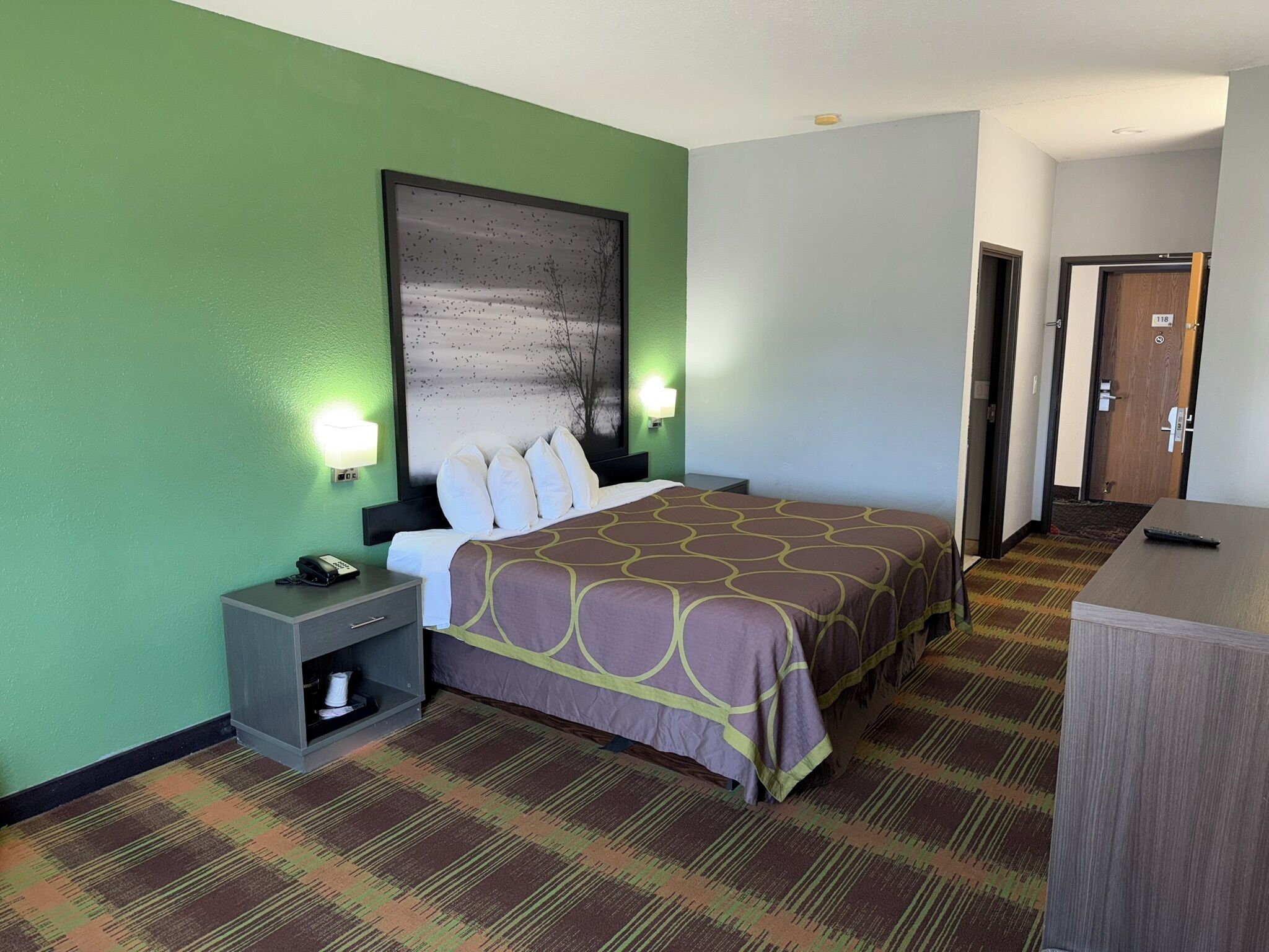 Camera d'albergo con un letto, comodini, una scrivania, un quadro di grandi dimensioni e pavimento con tappeto.