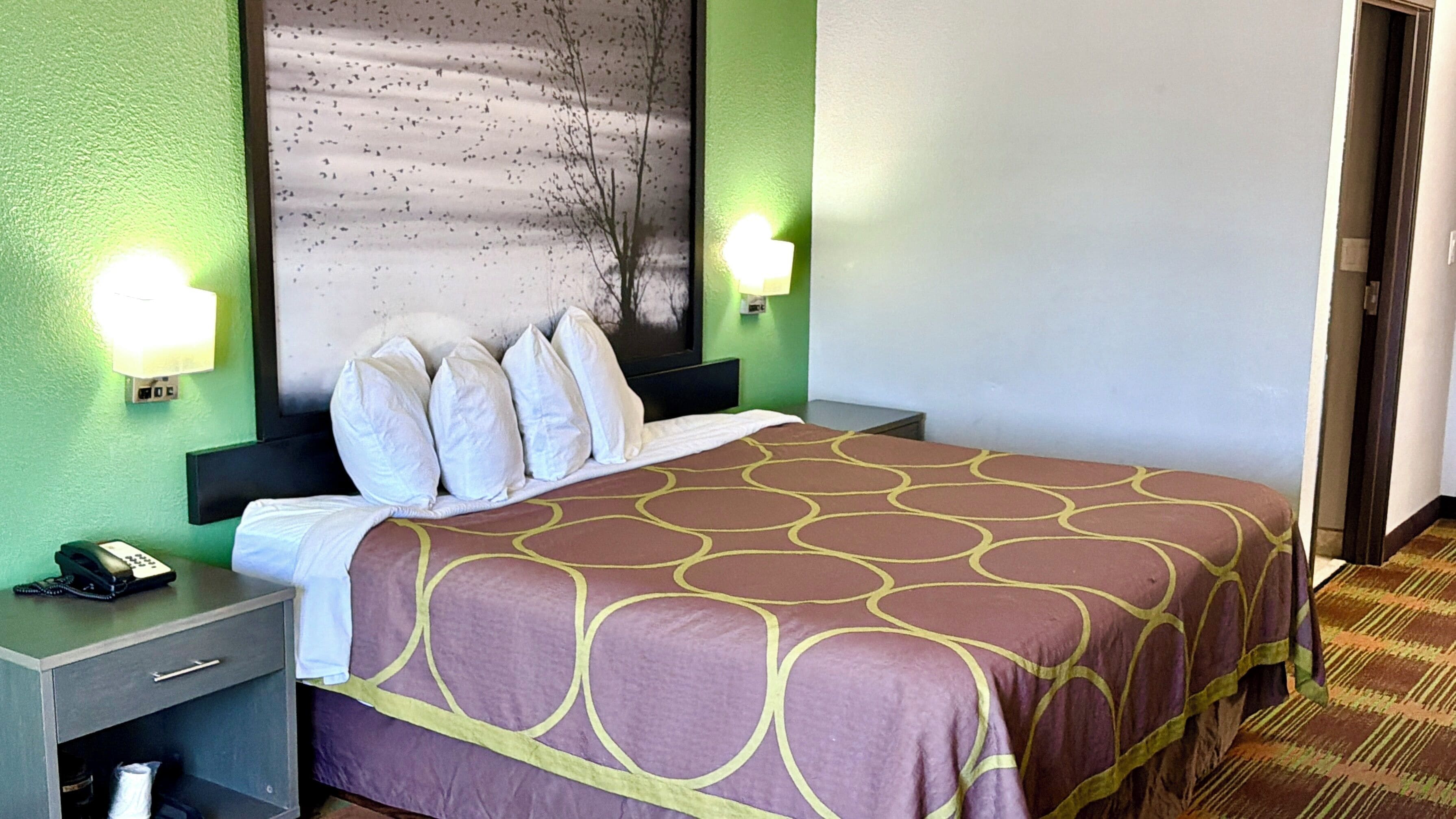 A hotel room with a bed, nightstands, a telephone, and wall-mounted lamps.