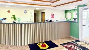 A hotel reception area with a reception desk, a ceiling fan, a fire extinguisher, and a green wall. - Super 8 by Wyndham Sweet Springs (Sweet Springs)