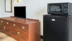 A hotel room with a wooden dresser, a flat-screen TV, and a black refrigerator with a microwave on top. - Super 8 by Wyndham Sweet Springs (Sweet Springs)