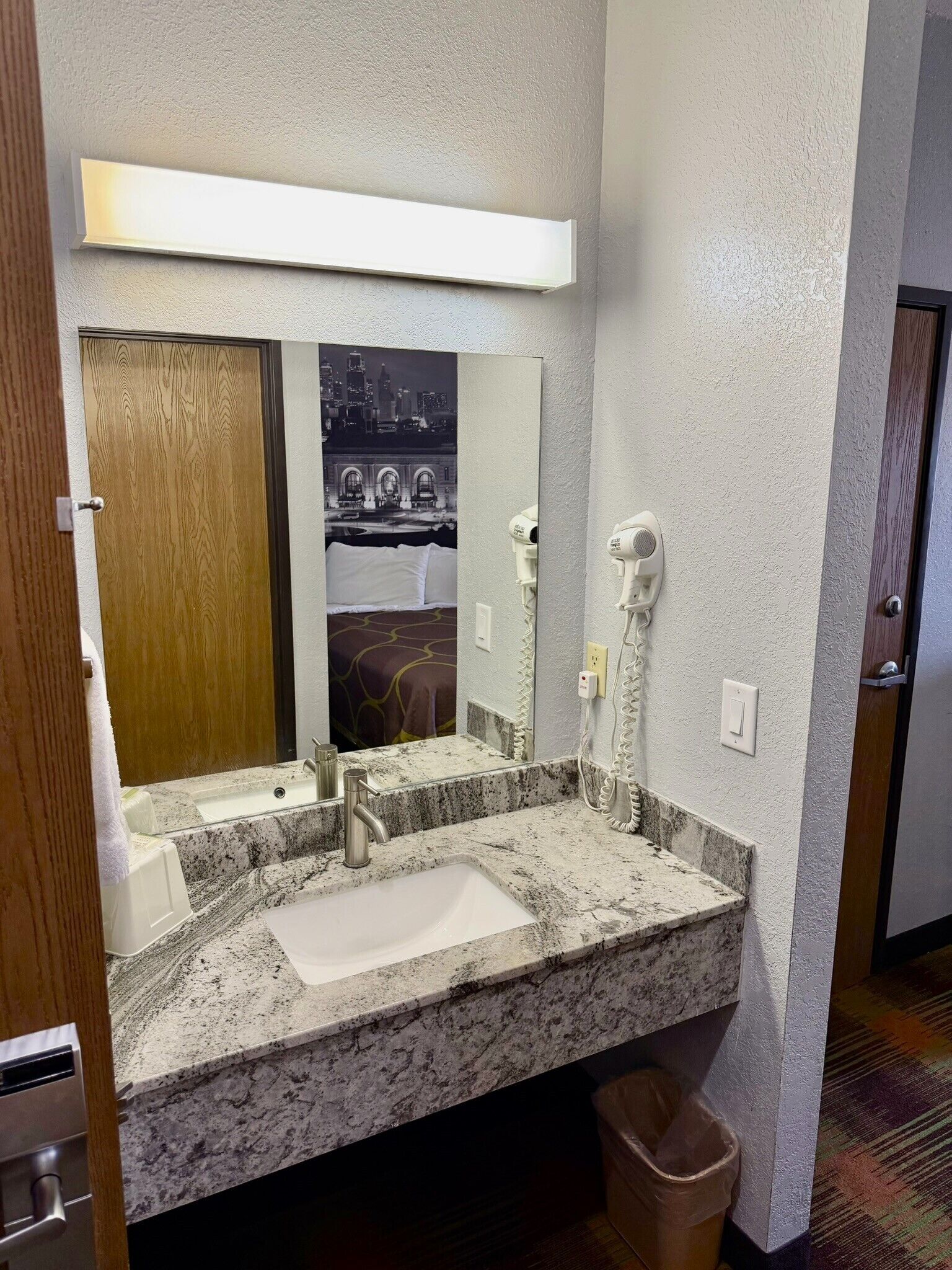A hotel bathroom with a granite sink, a mirror, a hairdryer, and a towel rack.