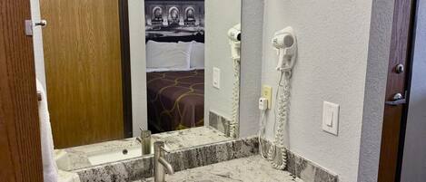 A hotel bathroom with a granite sink, a mirror, a hairdryer, and a towel rack.